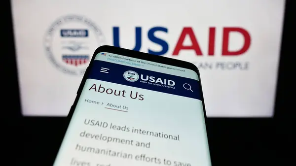 Smartphone with website of United States Agency for International Development (USAID) in front of logo. Focus on top-left of phone display.